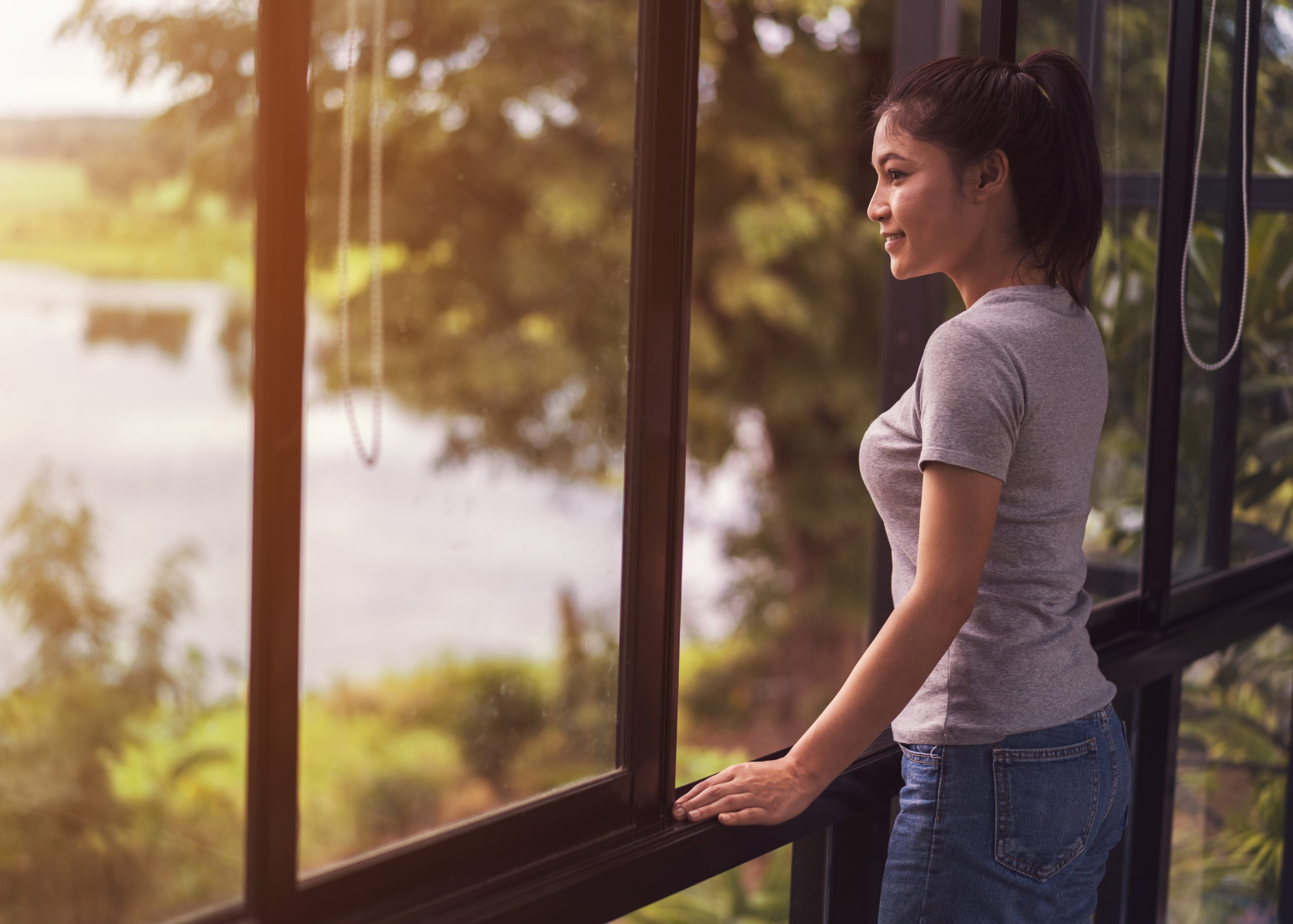 Young woman looking through window at a lake. Link takes you to the Bank of Versailles Checking and Savings Accounts page.